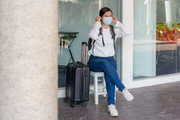 Traveling. Woman in a white long-sleeved shirt and jeans, wearing a mask. sit on the chair during...