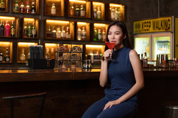 Nightlife concept a pretty girl with long hair wearing blue dress holding a pink drink appreciating...