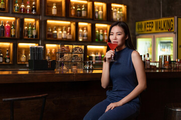 Nightlife concept a pretty girl with long hair wearing blue dress holding a pink drink appreciating the musics alone in the bar