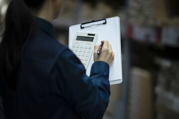 Warehouse worker checking inventory with calculator in logistics warehouse - Powered by Adobe