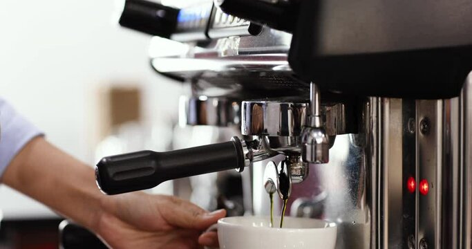 Barista using finger press on start button to make cup of coffee.