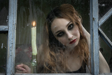 Beautiful sad young girl looking out the window with a candle