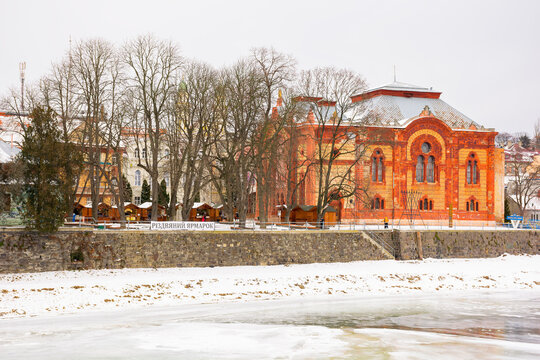 uzhgorod, ukraine - JAN 09, 2017: winter holidays in old town. embankment in snow and river uzh covered with ice. red building of old synagogue
