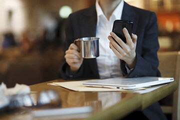 Businesswoman reading news on smartphone and drinking coffee in cafe	