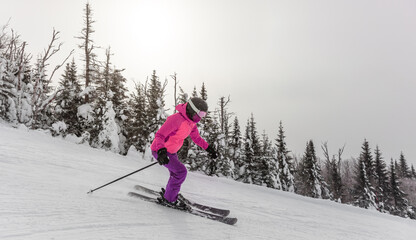 Skier woman skiing downhill on white snow fast down the mountain slope with tree landscape wearing...