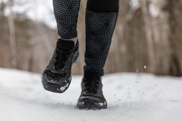 Winter running shoes woman training cardio outdoors jogging on white snow in cold weather. Closeup of feet wearing fitness footwear.