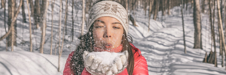 Winter Asian young woman blowing on snow for fun playing outdoor in nature forest. happy girl banner panoramic wearing cold weather accessories.