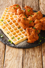 Fried Breaded Chicken pieces and Belgian waffles with creamy honey sauce close-up on a slate board on the table. vertical