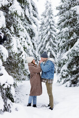 Fototapeta na wymiar lovely couple standing in winter forest, holding hands and blowing to keep warm in the cold