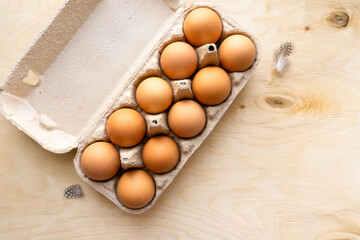 Raw brown chicken eggs in cardboard box on wooden background, top view