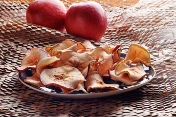 Dried apple chips in rustic plate and two red apples. Soft focus.