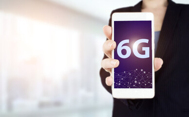 The concept of 6G network, high-speed mobile Internet, new generation networks. Hand hold white smartphone with digital hologram 6G sign on light blurred background. Global world telecommunication