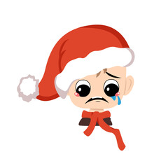 Boy with crying and tears emotion, sad face, depressive eyes in red Santa hat. Cute kid with melancholy expression in carnival costume for New Year, Christmas and holiday. Head of adorable child