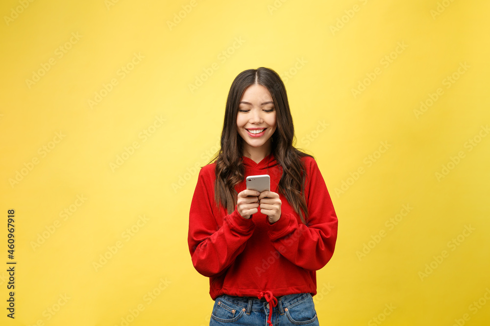 Wall mural Young beautiful happy woman using smart phone. Isolated on yellow background