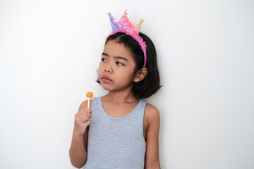 Asian little kid glancing to her side with annoyed face expression while holding lolipop candy