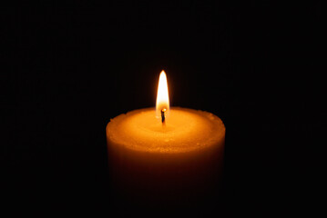 One single light candle burning brightly in the black background.Spiritual candle yellow flame. Flame of candle in the darkness.Copy space.