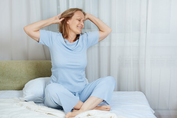 Fototapeta na wymiar smiling senior woman in blue pajamas stretching in the morning after sleeping in her bed.