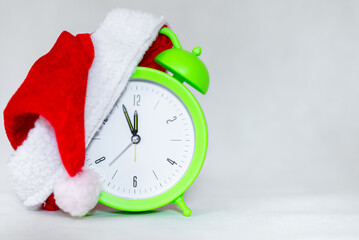 Alarm clock with Santa hat isolated on gray white background.Green clock with christmas red santa...