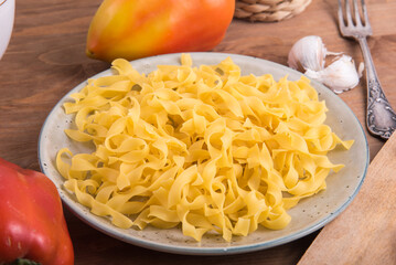 Raw noodles in a plate on a wooden table with peppers for a simple dish