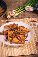 Fried tofu in a plate with hot sauce with onions and sesame seeds