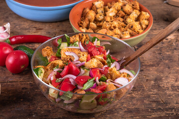 Cooking tomato, onion and cucumber panzanella salad with toasted ciabatta pieces. Ready mixed vegetable salad with croutons in a glass bowl