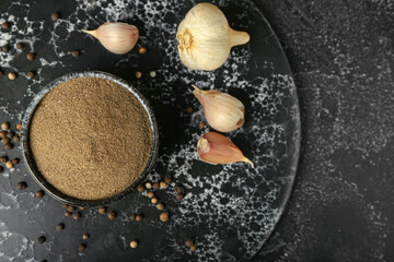 Bowl with black pepper powder and garlic on dark background