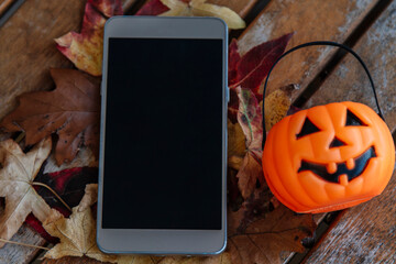 mobile phone on dry leaves and pumpkin. autumn and halloween concept