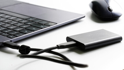 An external portable SSD drive connected to a laptop on a white background next to a computer...