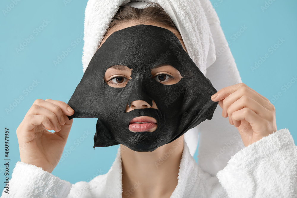 Wall mural Beautiful young woman with sheet facial mask on color background