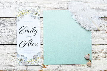Blank card with text EMILY & ALEX, earrings and feather on white wooden background