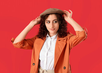 Young Parisian woman adjusting stylish beret hat on red background