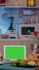 Couple looking at horizontal green screen on tablet while eating meal at festive dinner on christmas eve. Cheerful people watching chroma key with isolated mockup template enjoying festivity