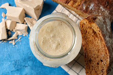 Glass jar with fresh sourdough and bread on blue background