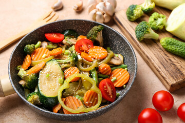Frying pan with different vegetables on color background, closeup