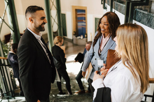 Cheerful male professional discussing with female colleagues while standing on staircase at convention center