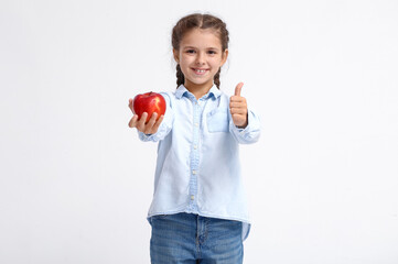 Little girl with apple showing thumb-up on white background