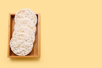 Wooden box with puffed rice crackers on color background
