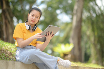 Teenage girl wearing headphones on neck holding tablet looking at camera serious expression.