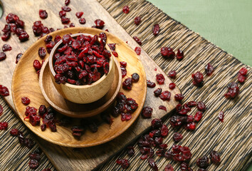 Bowl with tasty dried cranberries on color wooden background, closeup