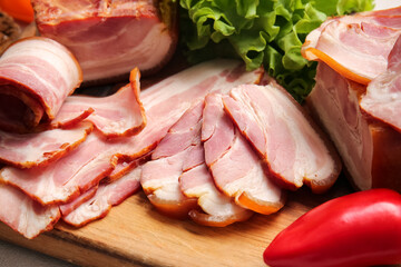 Wooden board with tasty slices of tasty smoked bacon on table, closeup