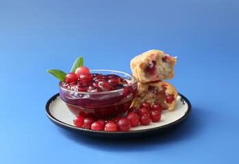 Bowl with tasty cranberry jam, berries and muffin on blue background