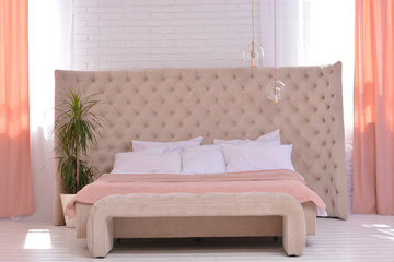 Stylish elegant bed in the bedroom against the background of a white brick wall near the windows with a flower and beautiful decoration.Copy space for text