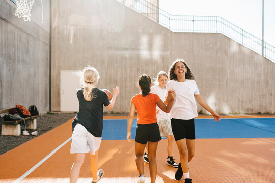Happy female friends holding hands while walking in basketball court