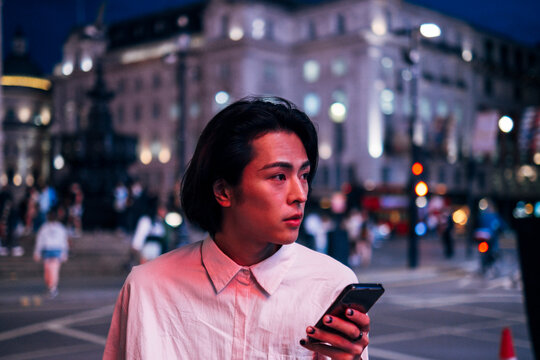 Handsome man with black hair holding mobile phone in city