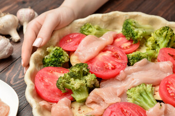 Female hands with uncooked chicken pot pie on wooden background, closeup