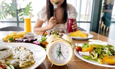 Selective focus of Alarm yellow clock  which young woman  enjoy eating of food  and Intermittent fasting diet concept in the kitchen
