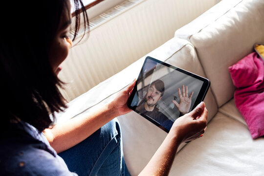 Mid adult woman talking on video call with male friend through digital tablet in living room