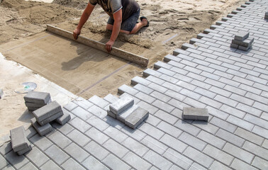 A worker lays down sand for paving slabs.