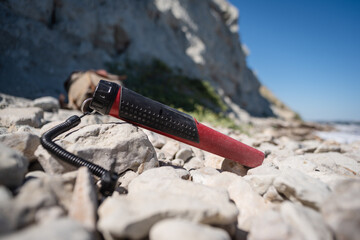 Naklejka premium A pin pointer metal detector in the sea beach pebbles close up. Summer hobby.