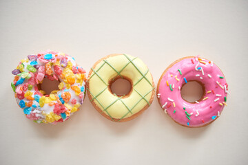 Directly above view of three multi-colored doughnuts with frosting and sprinkles against isolated background